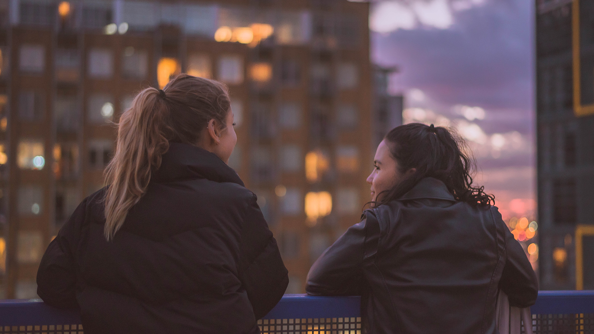 two women looking at each other in front of a city skyline
