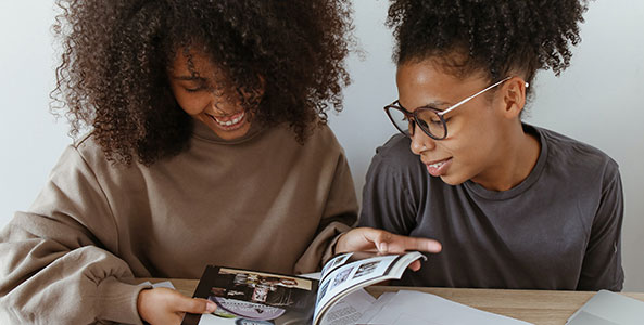 two women smiling as they look at a magazine